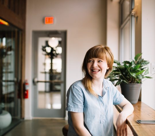 A smiling woman leaning on a wooden ledge