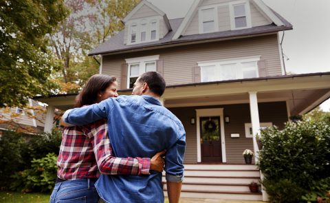 Une femme et un homme dans les bras l’un de l’autre devant une maison