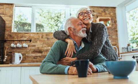 An elderly woman hugging an elderly man in a kitchen