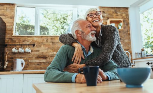 An elderly woman hugging an elderly man in a kitchen