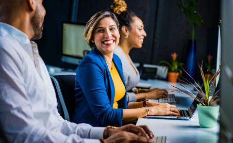 A woman smiling at her colleagues and typing on her laptop