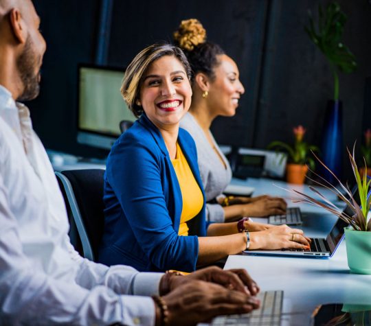 A woman smiling at her colleagues and typing on her laptop