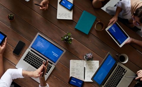 Aerial view of a conference table with people, laptops, notebooks and phones