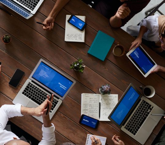 Aerial view of a conference table with people, laptops, notebooks and phones