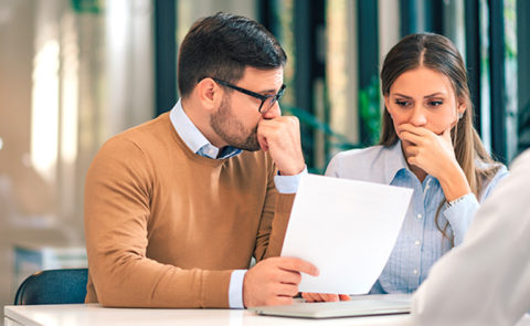 Portrait of a couple with financial problems looking at document in financial adviser's office.