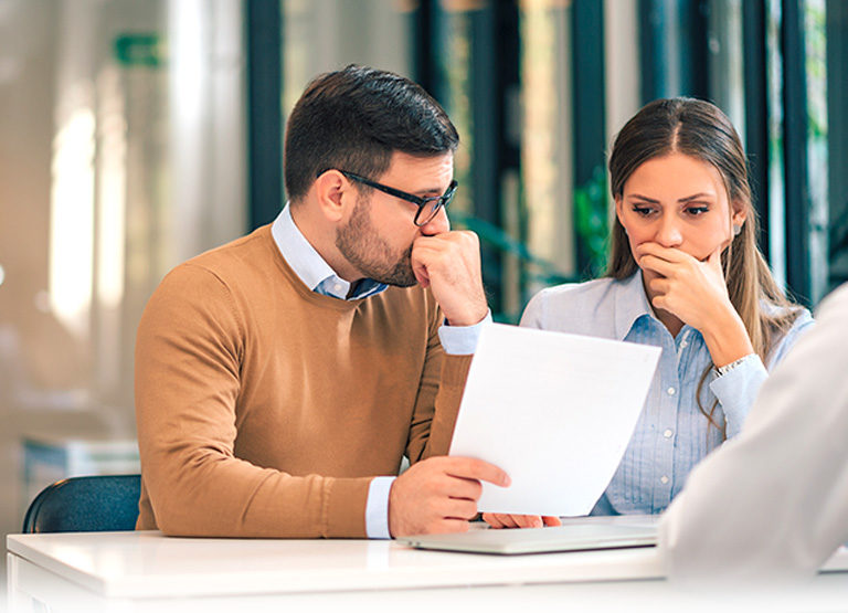 Portrait of a couple with financial problems looking at document in financial adviser's office.