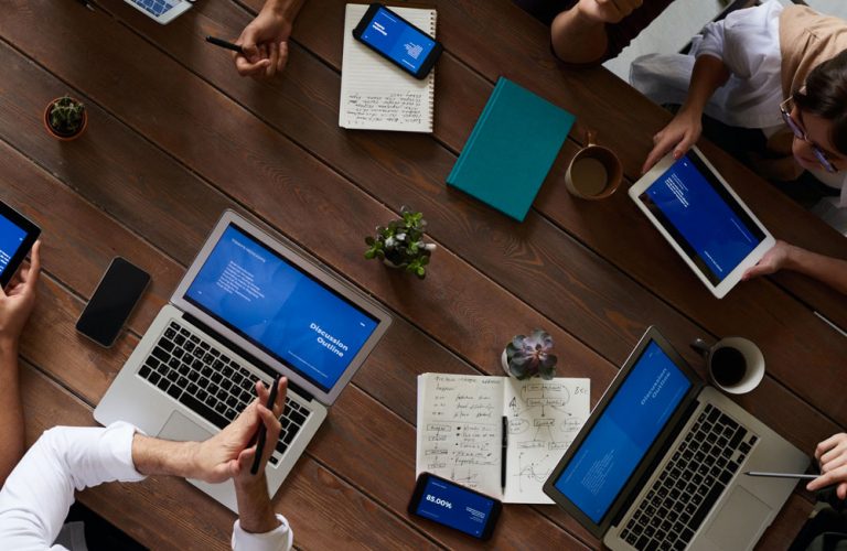 Aerial view of a conference table with people, laptops, notebooks and phones